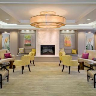 A modern lobby with a central fireplace, surrounded by seating and artwork, featuring a large chandelier.
