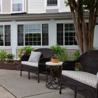 A cozy outdoor seating area with chairs and a table, surrounded by plants in front of a building.