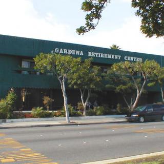 A business building with signage reading 'Gardena Business Center' on a street lined with trees.