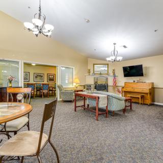 A spacious living room featuring comfortable seating, a TV, and a piano, illuminated by elegant chandeliers.