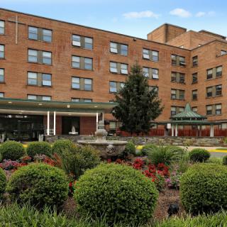 A brick hospital building with a well-maintained garden in the foreground.