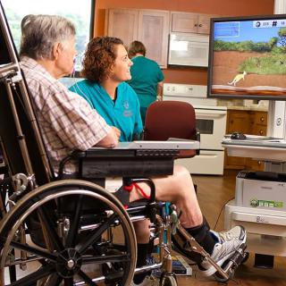 An elderly person in a wheelchair participates in physical therapy with the assistance of a healthcare professional.