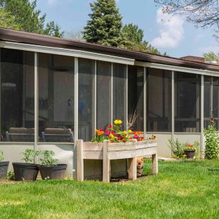 A serene backyard featuring a screened porch with a raised planter filled with flowers and greenery.