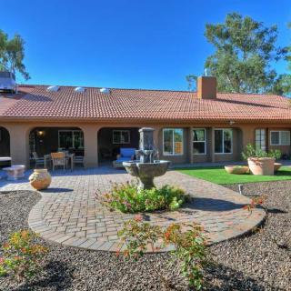 A beautiful house with a spacious patio and garden area, featuring outdoor furniture and a central fountain under a clear blue sky.