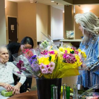 Elderly woman receiving visitors in a nursing home with vibrant bouquets of flowers around.