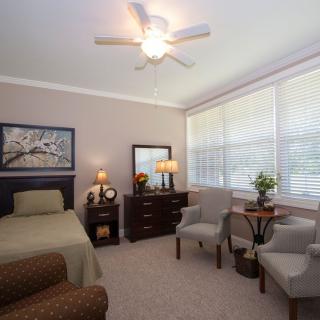 A cozy bedroom with a single bed, dresser, and seating area by large windows.