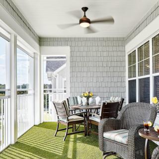 A cozy porch with wicker furniture and a ceiling fan, illuminated by natural light through glass doors.