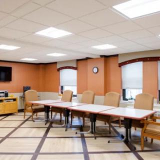 An empty conference room with a large table, surrounded by chairs and featuring a wall-mounted television and clock.