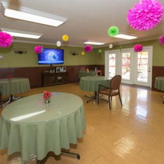 A brightly decorated dining room featuring tables with green tablecloths and colorful pompoms hanging from the ceiling.
