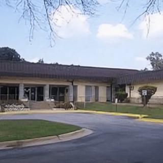 A one-story building with a paved driveway and well-maintained lawn under a clear sky.
