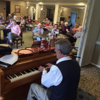 A musician plays the piano for an audience in a cozy indoor setting.