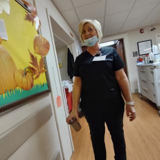 A healthcare worker in a hospital corridor, wearing a mask and black scrubs.