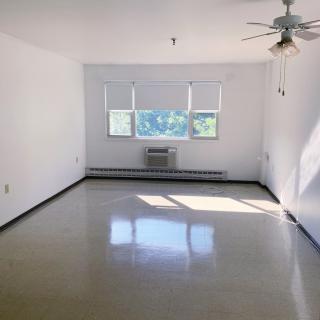 A minimalist empty room with plenty of natural light coming through a window, featuring a ceiling fan.