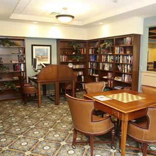 A cozy library with bookshelves, a reading area, and a chess table.