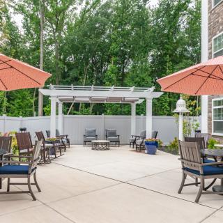 A cozy outdoor patio with seating arrangements under large umbrellas, surrounded by trees and a pergola.