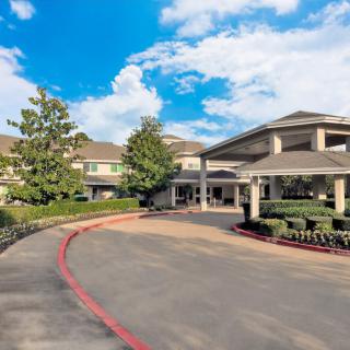 A well-maintained residential building with a circular driveway and landscaped surroundings under a partly cloudy sky.