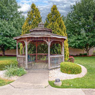 A charming gazebo nestled in a lush garden, surrounded by vibrant greenery and a serene pathway.