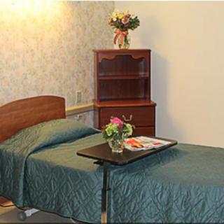 A cozy bedroom with a single bed, bedside table, and a shelf holding flowers. A tray with a magazine and vase is placed on the bed.