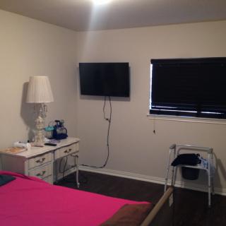 A bedroom with a wall-mounted television, nightstand, and window blinds.