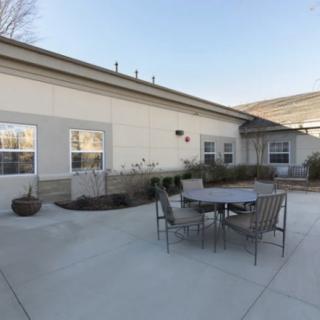 A view of an outdoor patio area with metal chairs and a table on a concrete surface next to a building.