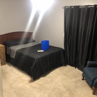 A bedroom with a bed, nightstand, chair, and dark curtains.