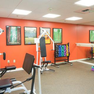 A bright gym room featuring various fitness equipment against orange walls.