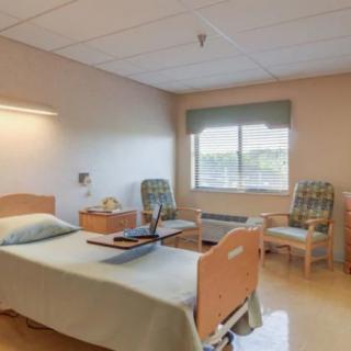 A clean and organized hospital room with a bed, chairs, and a window.