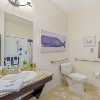 A well-lit bathroom featuring a toilet, sink with a mirror, and whale-themed decor.