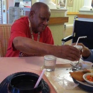 An elderly man enjoying a meal at a restaurant, sharing a drink with someone.