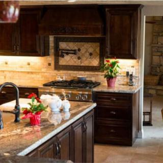 A modern kitchen with dark wood cabinets and granite countertops, featuring a stove and decorative plants.