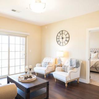 A bright living room with two armchairs, a coffee table, and a wall clock.