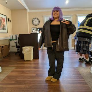 A person with purple hair in a casual outfit strikes a playful pose indoors.