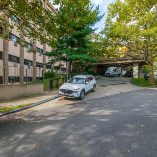 A car parked near a residential building with a driveway surrounded by trees.