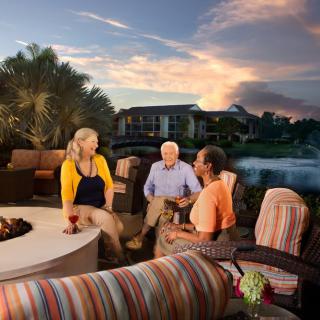 A group of people enjoying a conversation by the fire pit on a patio during sunset.