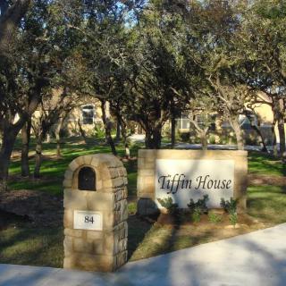 An outdoor entrance with a sign reading 'Tijon House' surrounded by trees.