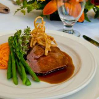 A gourmet steak dish served with asparagus, onion rings, and a savory sauce.
