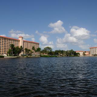 A scenic view of buildings by the lakeside under a clear blue sky with fluffy clouds.
