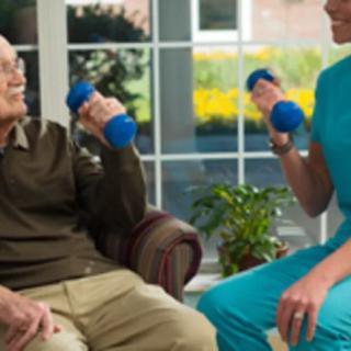 A healthcare professional assists an elderly person with light weightlifting exercises.