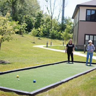 Two individuals playing bocce on a well-maintained lawn.