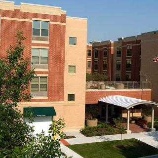 A multi-story residential building with a brick exterior, featuring an entrance with a canopy and well-maintained landscaping.