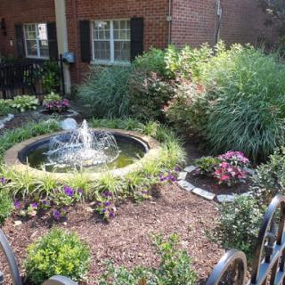 A serene garden featuring a central fountain surrounded by lush plants and colorful flowers.