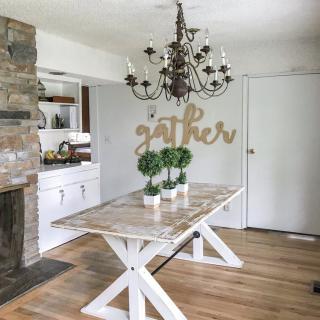A modern farmhouse dining room featuring a wooden table, elegant chandelier, and a welcoming 'gather' sign on the wall.