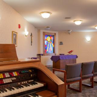 A peaceful chapel interior featuring an organ and a colorful stained glass window.