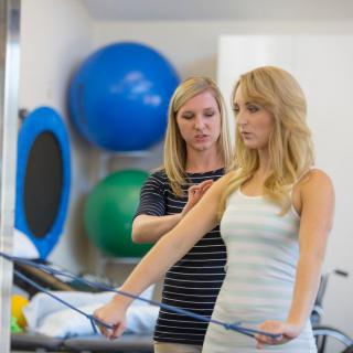 A therapist guides a patient through an exercise using resistance bands in a rehabilitation setting.