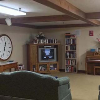 A cozy living room with a large wall clock, bookshelves, and an old-fashioned TV.