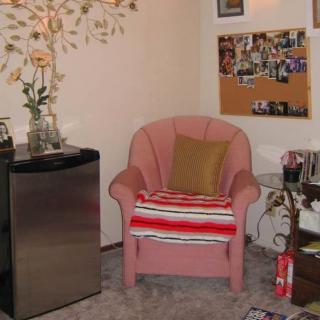 A cozy corner with a cushioned chair adorned with a blanket, beside a bulletin board displaying photos.