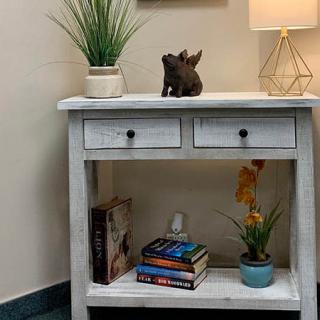 A decorative white table with drawers, topped with a lamp and plants, books below.