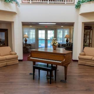 A spacious living room with a grand piano at the center, surrounded by sofas and elegant decor.