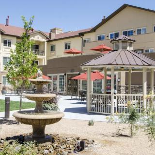 A sunny outdoor area with a fountain, gazebo, and seating with umbrellas.