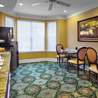 A cozy dining area with a round table and chairs, featuring a patterned carpet and large windows.